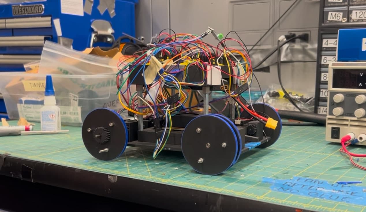 Four-wheeled transformable robot prototype on a workbench, wired to bench power supplies